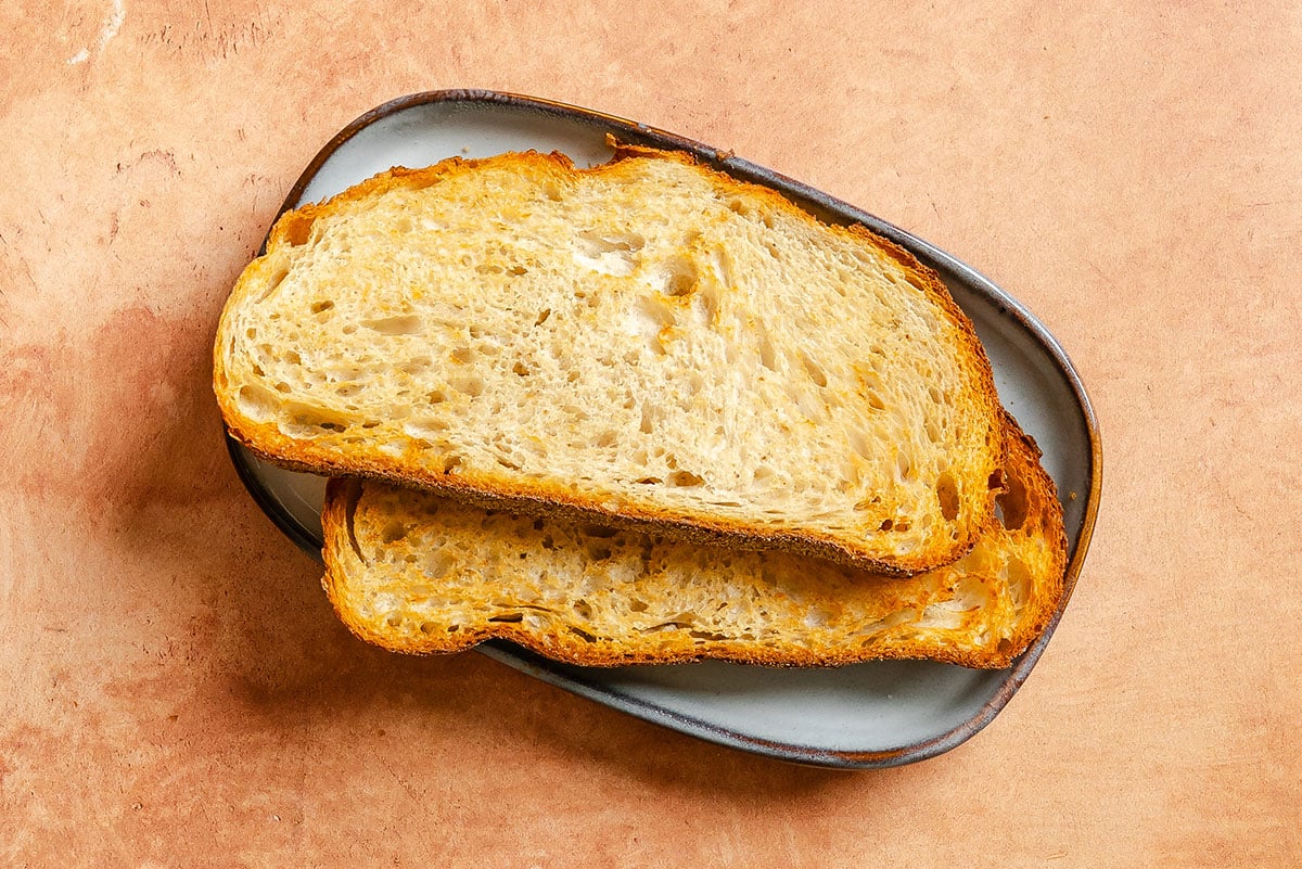 Two slices of toasted bread are stacked on a small gray plate placed on a light brown surface.