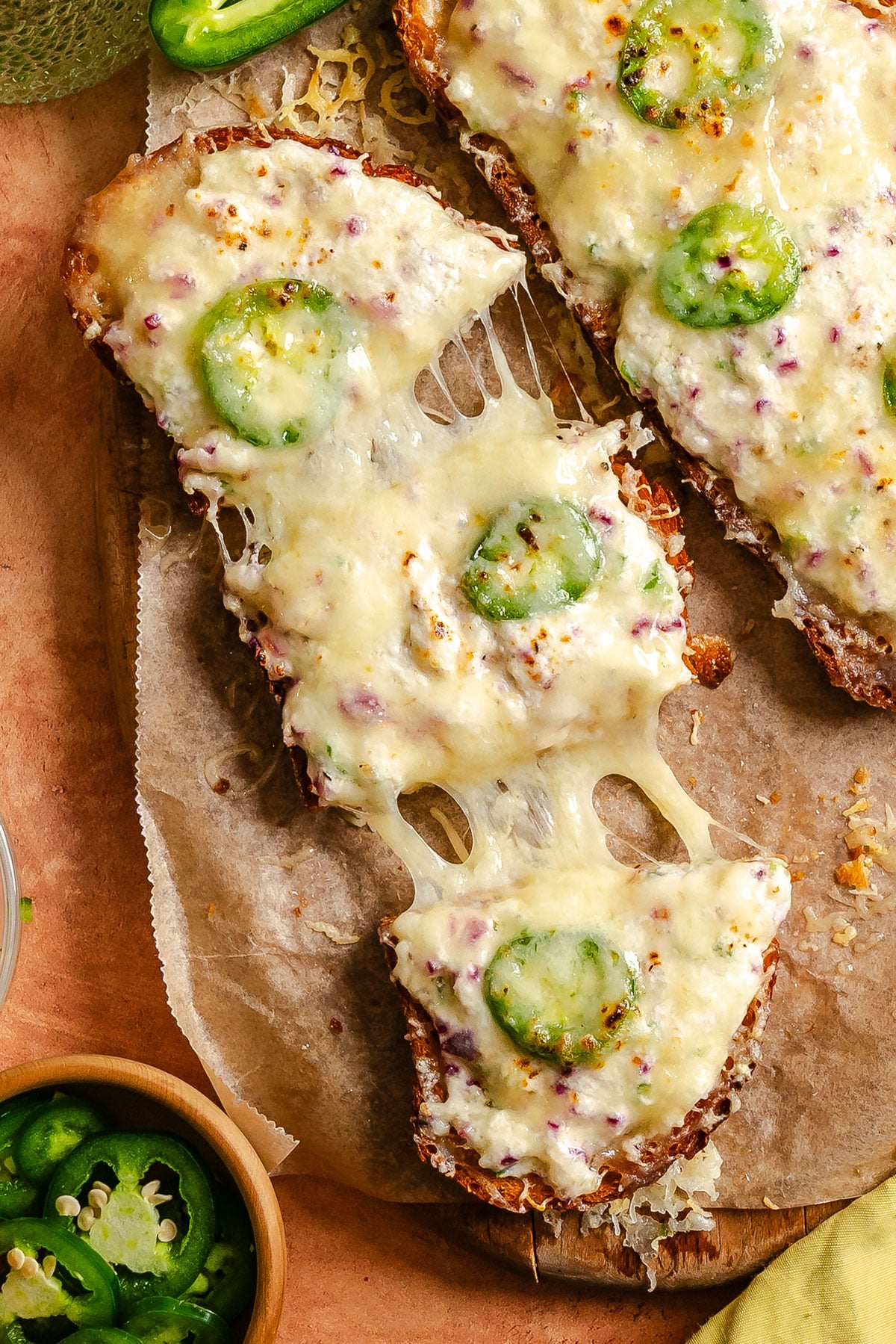 Toasted bread topped with melted cheese, round slices of jalapeño pepper, and bits of red onion on parchment paper.