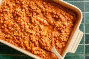 A baking dish filled with chickpea curry in a creamy tomato sauce, with a wooden spoon resting inside the mixture.