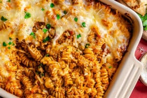 A close-up of a baked pasta dish with rotini, ground meat, tomato sauce, and melted cheese, garnished with chopped parsley in a rectangular casserole dish.