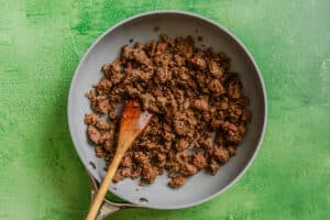 Cooked vegan ground beef in a frying pan with a wooden spatula, placed on a green surface.