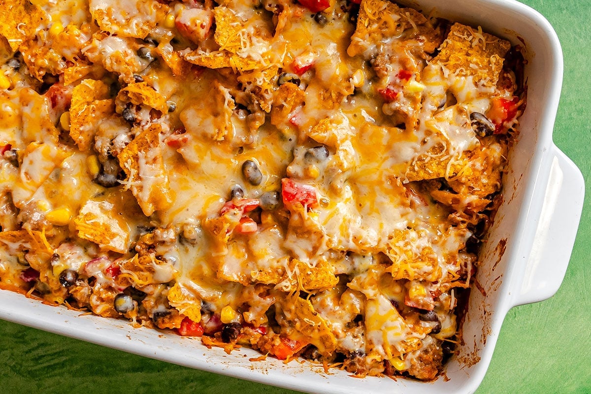 Baked vegetarian taco casserole in a white dish with melted cheese, tortilla chips, ground meat, black beans, corn, and diced tomatoes.