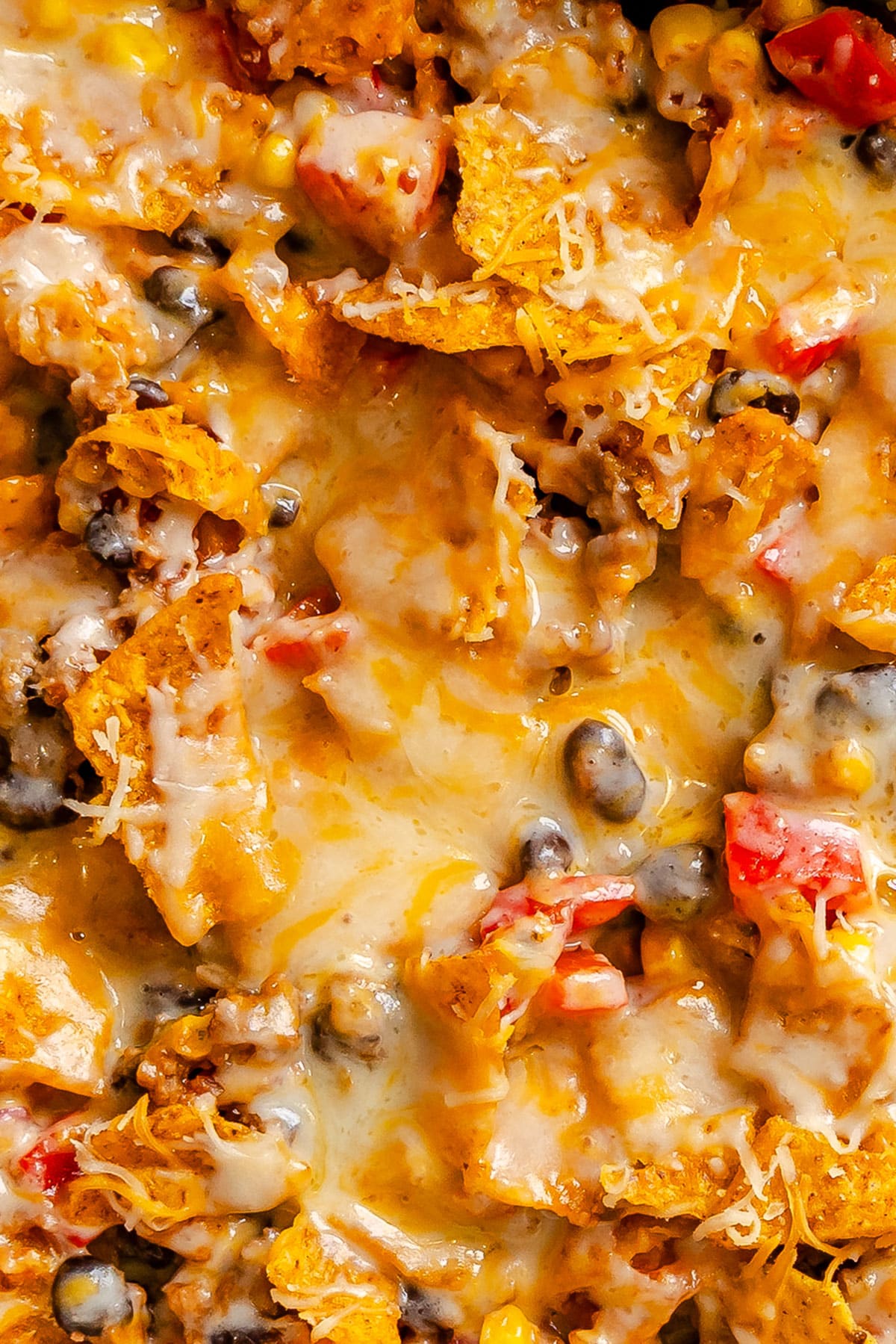Close-up of a cheesy nacho casserole with melted cheese, black beans, tortilla chips, ground meat, and diced red peppers.