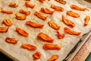 Sliced tomato pieces are arranged on a parchment-lined baking sheet, appearing roasted or dehydrated with some browning on the edges.