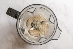 A blender containing finely ground oat flour sits on a light marble countertop, viewed from above.