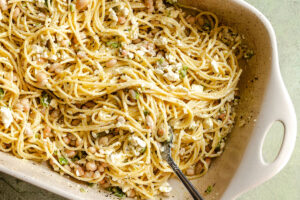 Baked spaghetti mixed with white beans, crumbled feta cheese, and herbs in a white ceramic dish with a serving fork.