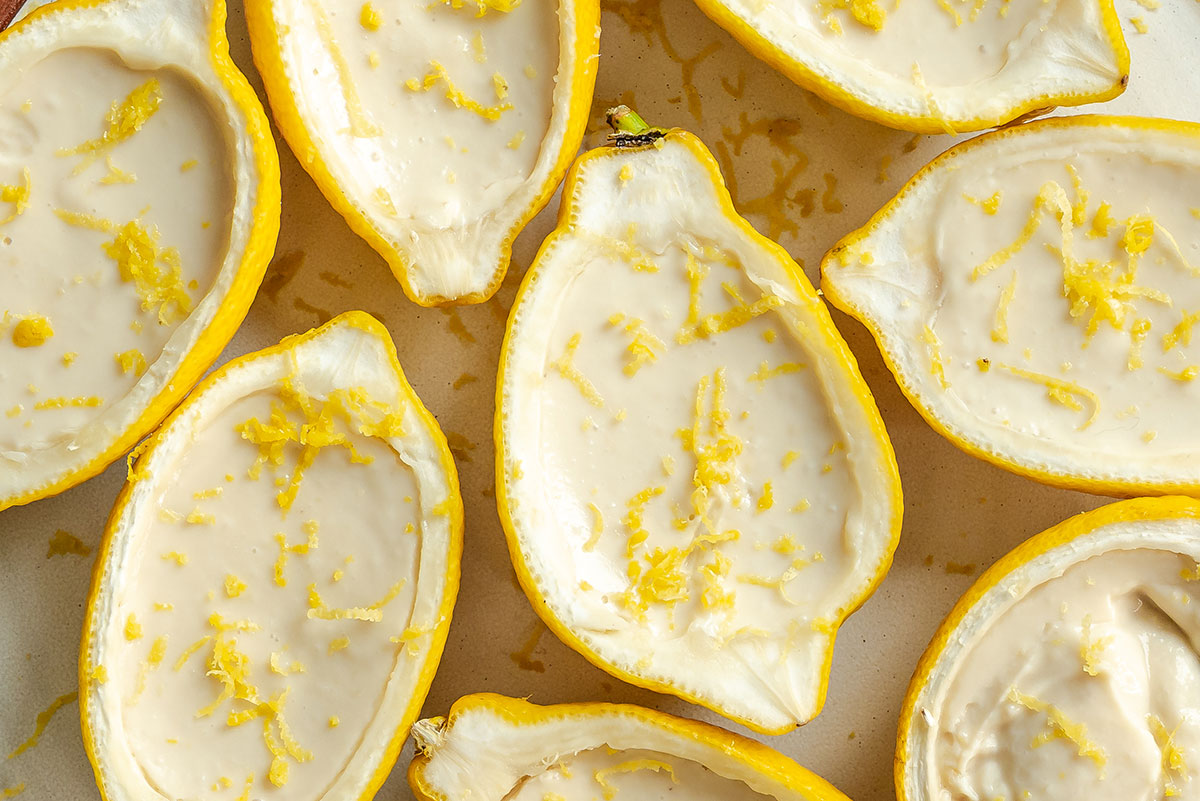 Halved lemons filled with a creamy dessert and topped with lemon zest, arranged closely together on a light surface.