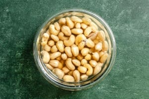 A glass bowl filled with soaked cashew nuts is placed on a green textured surface.