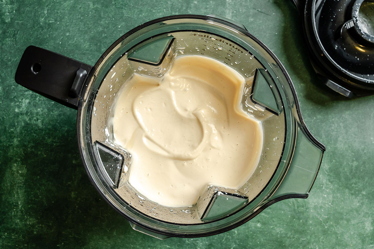 Top view of a blender containing a smooth, creamy light beige mixture, with some mixture on the sides of the blender jar.