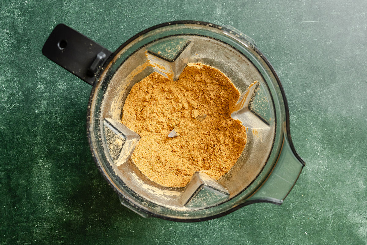 Top view of a blender containing a fine yellow-brown powder, set on a green textured surface.