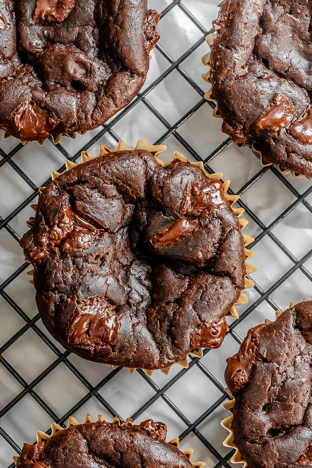 Chocolate muffins with visible chocolate chunks are cooling on a wire rack. The muffins have a rich, dark color and a slightly rough texture.