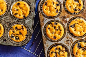 Two muffin pans filled with freshly baked chocolate chip muffins are resting on a wire rack.
