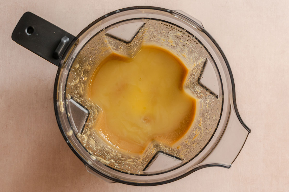 Top-down view of a blender containing a yellowish liquid mixture, with some residue on the sides of the container, placed on a light-colored surface.