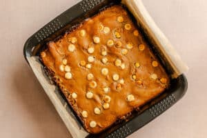 A square pan lined with parchment paper holds baked blondies topped with scattered white chocolate chips.