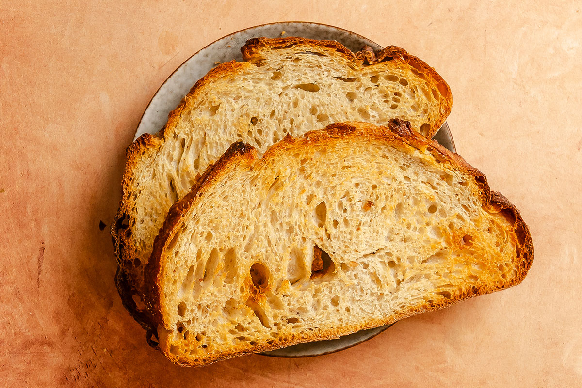 Two slices of toasted bread on a round ceramic plate, placed on a light brown textured surface.