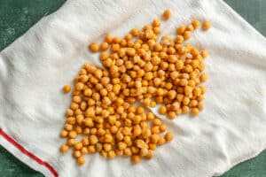Cooked chickpeas spread on a white kitchen towel with a red stripe, drying on a dark green surface.