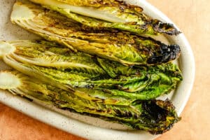 Grilled romaine lettuce halves arranged on a speckled oval plate, showing char marks and browned edges.
