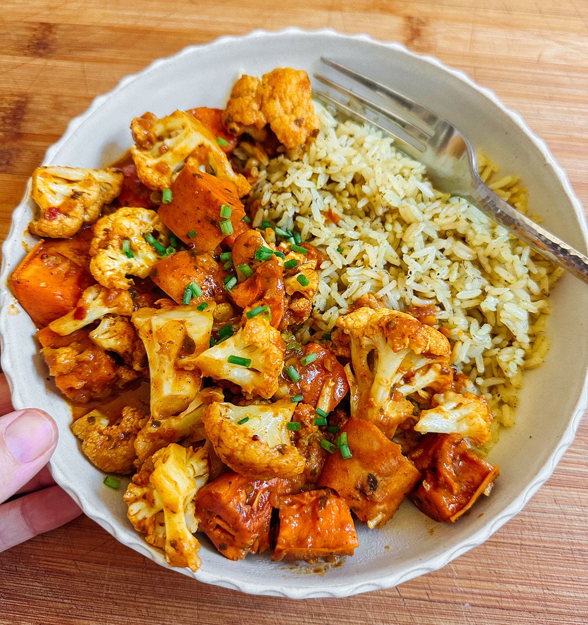 A bowl with roasted cauliflower and sweet potatoes next to a serving of seasoned rice, with a fork resting on the side.