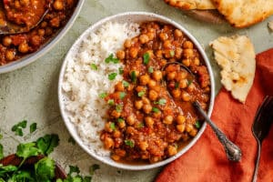 A bowl with white rice and chickpea curry garnished with cilantro, served with naan bread on the side and a spoon in the bowl.