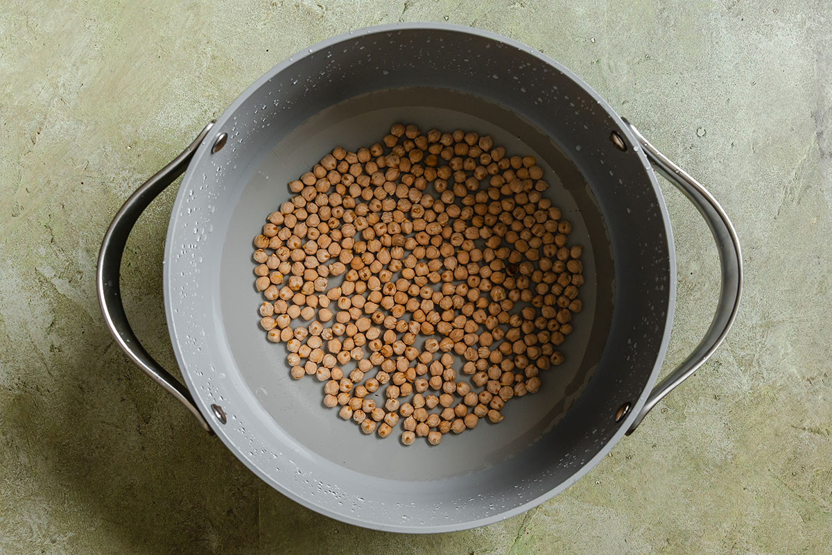 A gray pot filled with water and dried chickpeas sits on a green textured surface.