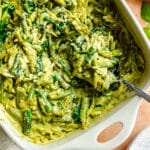 White dish filled with creamy orzo pasta mixed with spinach and green vegetables, with a metal spoon resting inside.