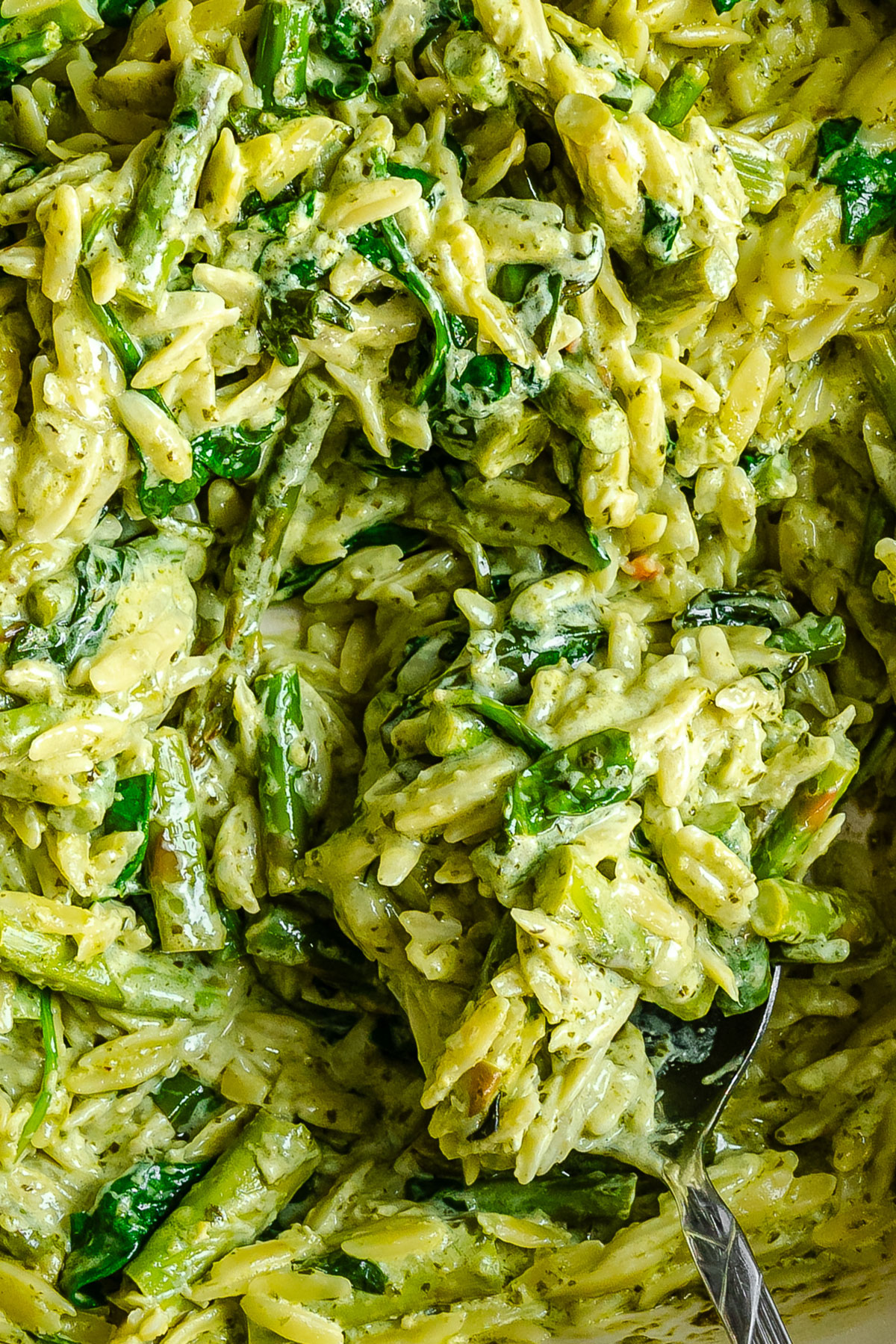 Close-up of creamy orzo pasta mixed with spinach and green vegetables, with a spoon partially visible.