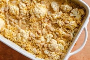 A white baking dish filled with cooked orzo pasta, large white beans, cauliflower florets, and a creamy sauce.