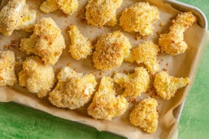 Breaded cauliflower florets are arranged on a parchment-lined baking tray, ready for baking.