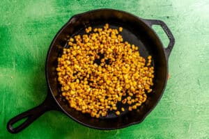 Charred corn kernels in a cast iron skillet on a green surface.
