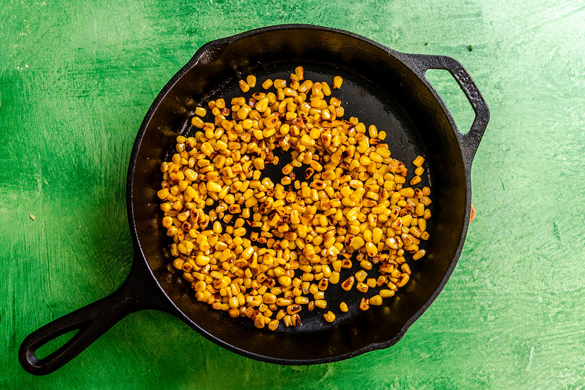 Charred corn kernels in a cast iron skillet on a green surface.