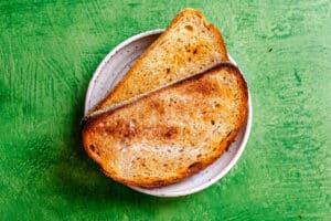 Two slices of toasted bread on a small white plate, viewed from above, placed on a green textured surface.