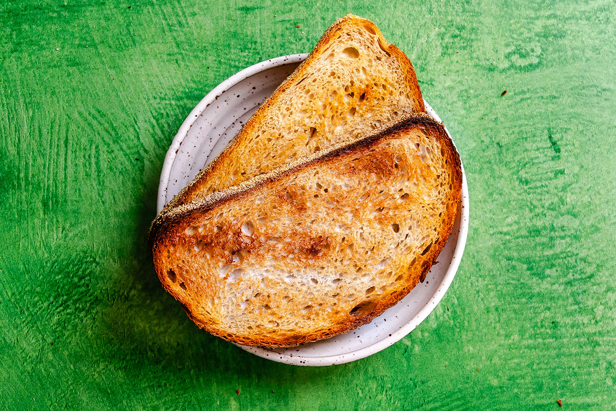 Two slices of toasted bread on a small white plate, viewed from above, placed on a green textured surface.