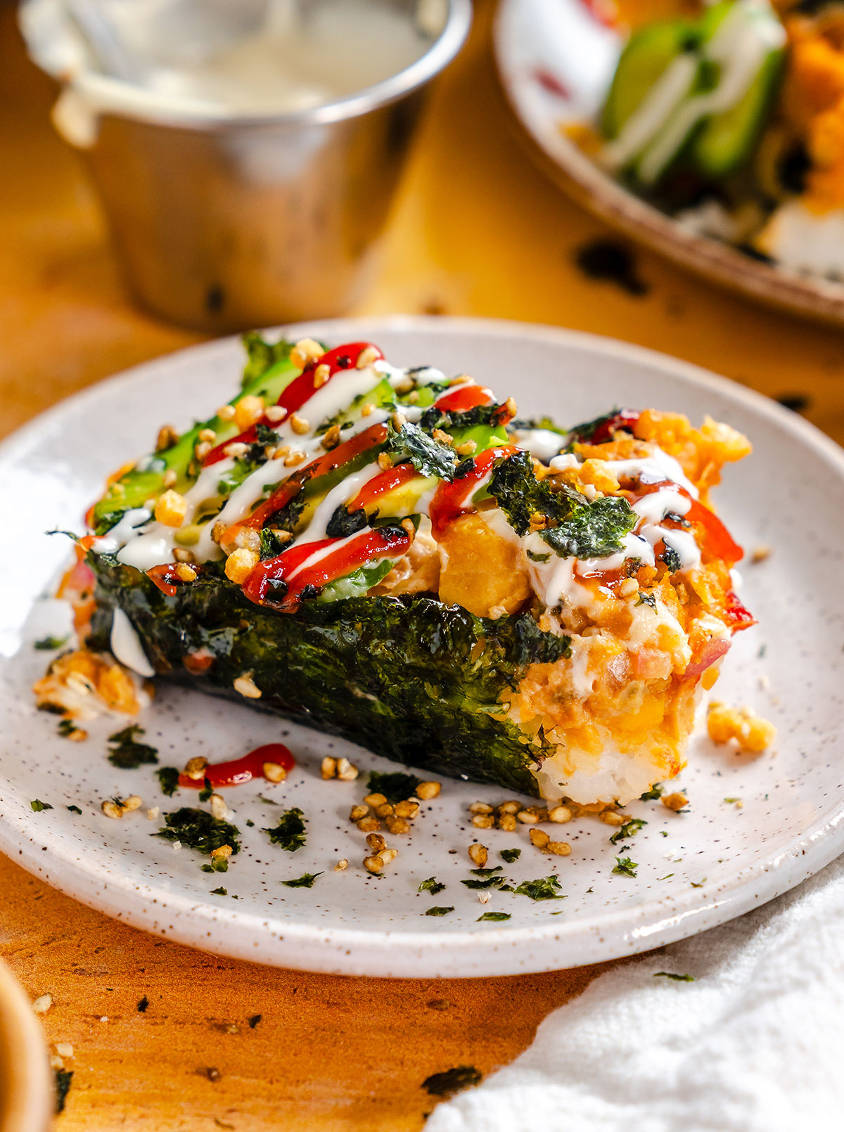 A plated sushi bake topped with seaweed, sauces, sesame seeds, and sliced green onions, served on a white ceramic plate.