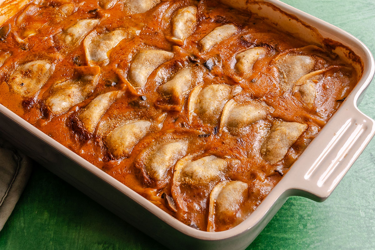 Rectangular baking dish filled with cooked dumplings or pierogi in a thick, reddish-brown sauce, arranged in overlapping rows on a green surface.