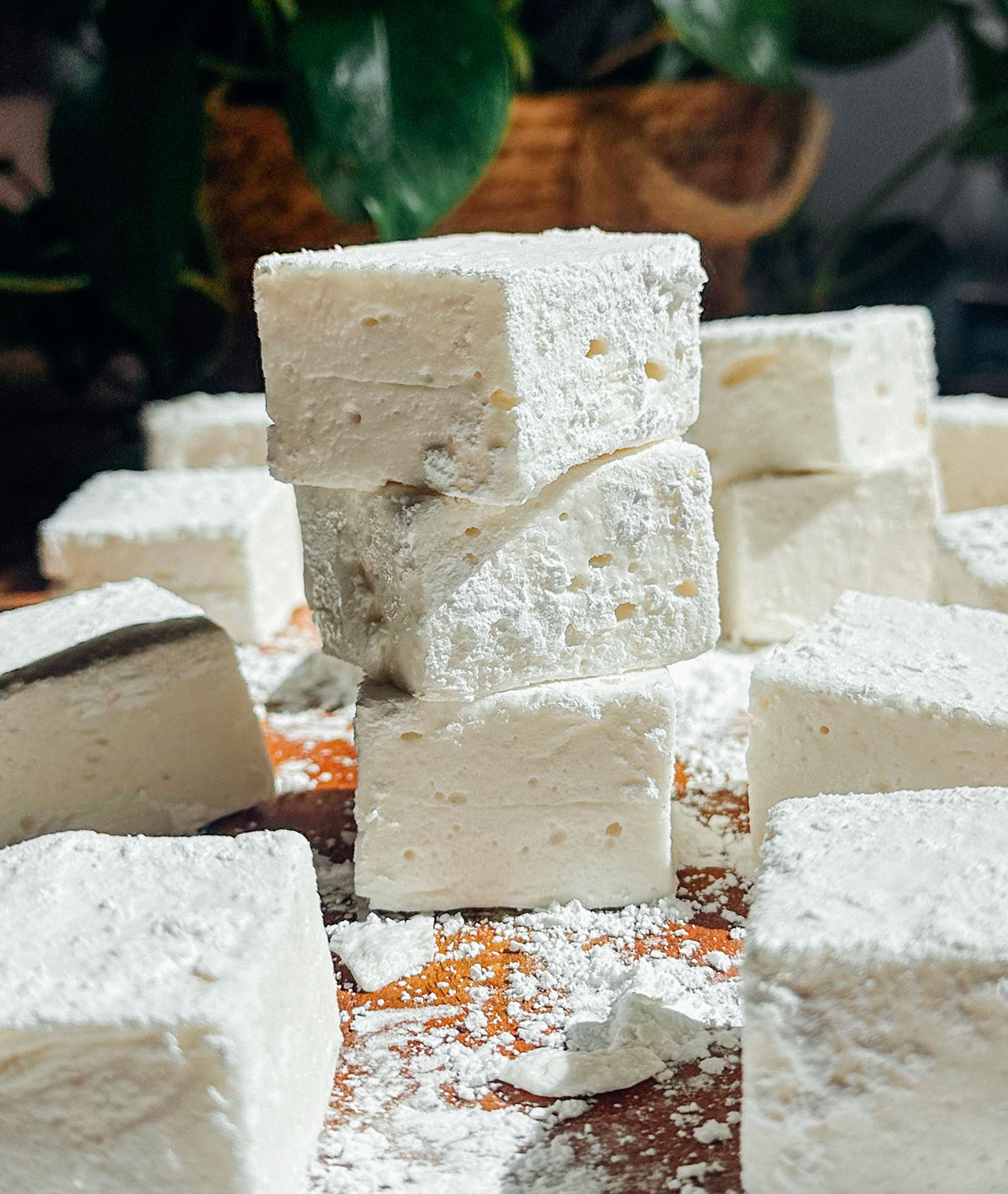 A close-up of several white marshmallows, with three pieces stacked in the center, all dusted with powdered sugar on a wooden surface.