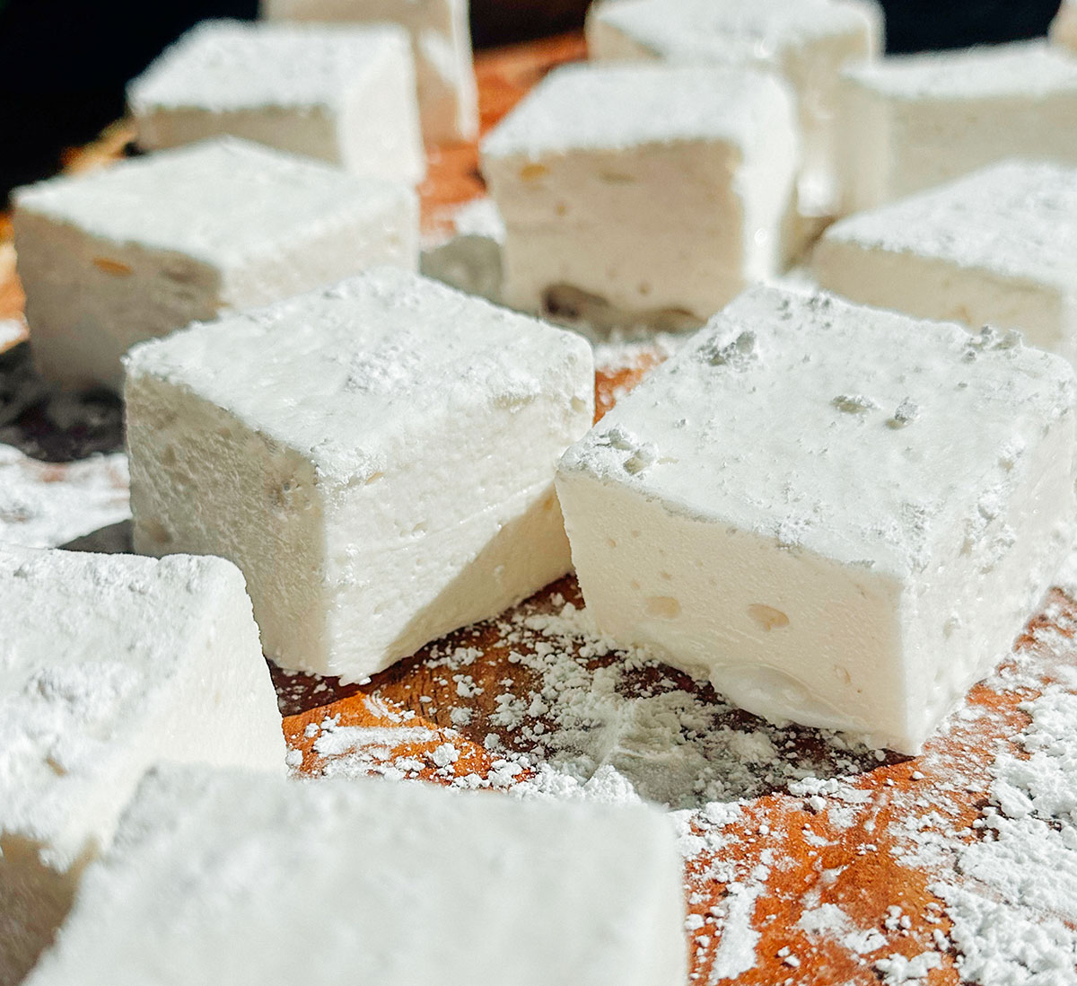 Close-up of several homemade marshmallows dusted with powdered sugar, arranged on a wooden surface.
