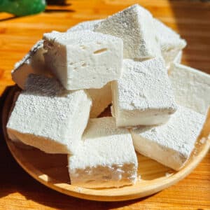 A small wooden plate holds several large white cubes of tofu, displayed in sunlight on a wooden surface.