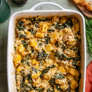 A casserole dish filled with a baked mixture of butternut squash, leafy greens, white beans, rice, and melted cheese makes for the perfect dump and bake Rice Casserole—wholesome comfort food that’s simple to prepare.