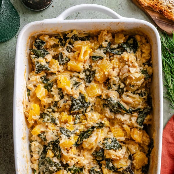A casserole dish filled with a baked mixture of butternut squash, leafy greens, white beans, rice, and melted cheese makes for the perfect dump and bake Rice Casserole—wholesome comfort food that’s simple to prepare.