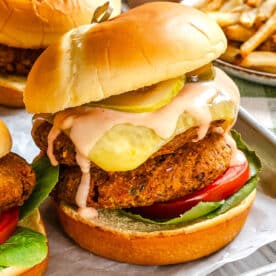A veggie burger with lettuce, tomato, pickles, and sauce on a bun sits on parchment paper. French fries are visible in the background.