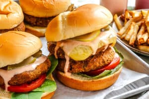 A close-up of veggie burgers with lettuce, tomato, pickles, and sauce on buns, next to a tray of French fries.