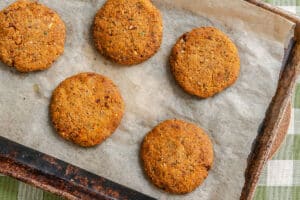 Five round, baked veggie patties on a sheet of parchment paper lined on a baking tray.