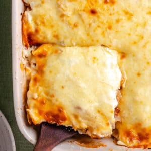 A baked cheesy casserole is being served from a rectangular dish with a wooden spatula.