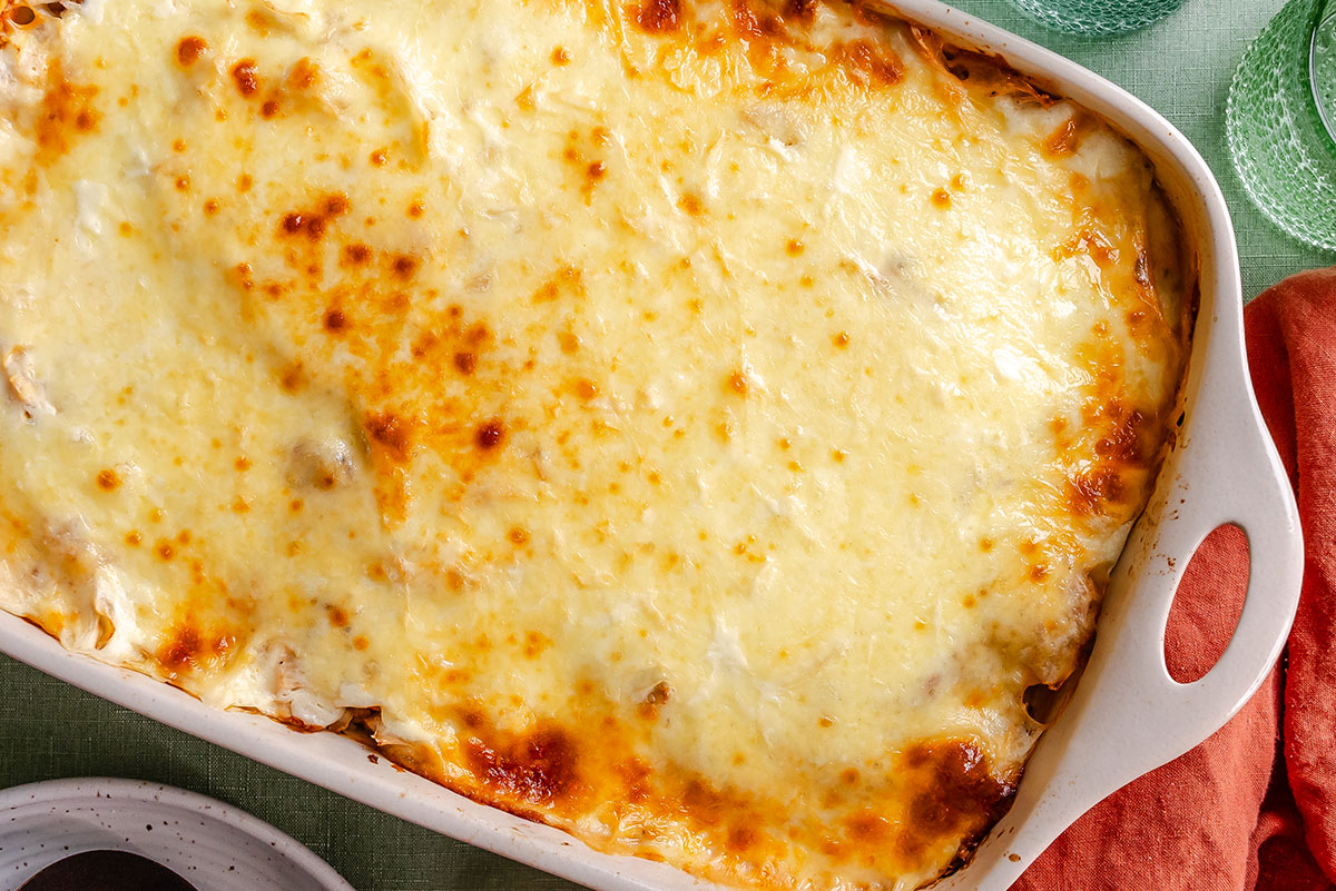 A baked casserole dish filled with a golden, bubbly layer of melted cheese, placed on a green surface next to an orange cloth and green glasses.