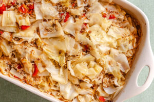 Casserole dish filled with baked cabbage, rice, tomatoes, and seasonings, viewed from above on a light-colored surface.