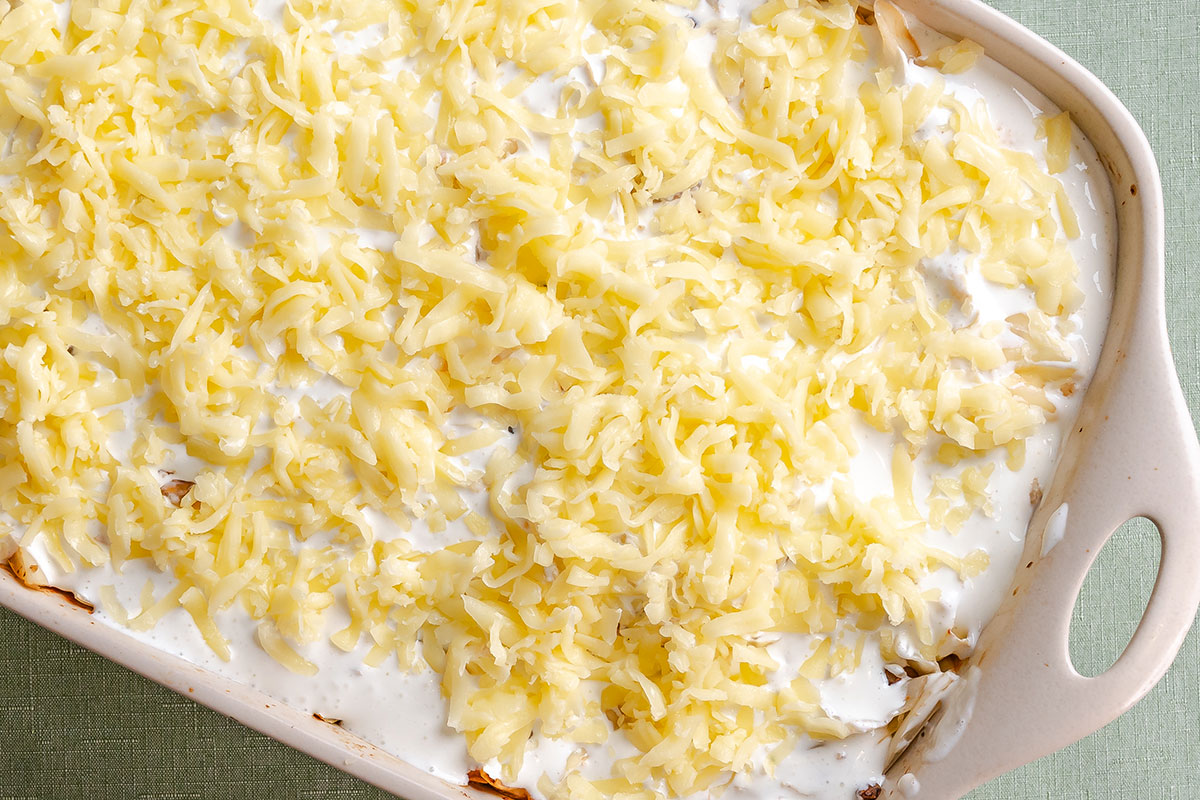 Casserole dish filled with an uncooked creamy mixture topped with a layer of shredded cheese.