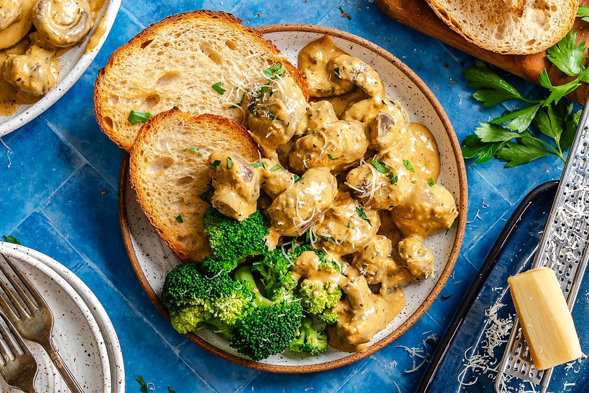 A plate with creamy mushroom sauce, steamed broccoli, and two slices of toasted bread, garnished with grated cheese and parsley.
