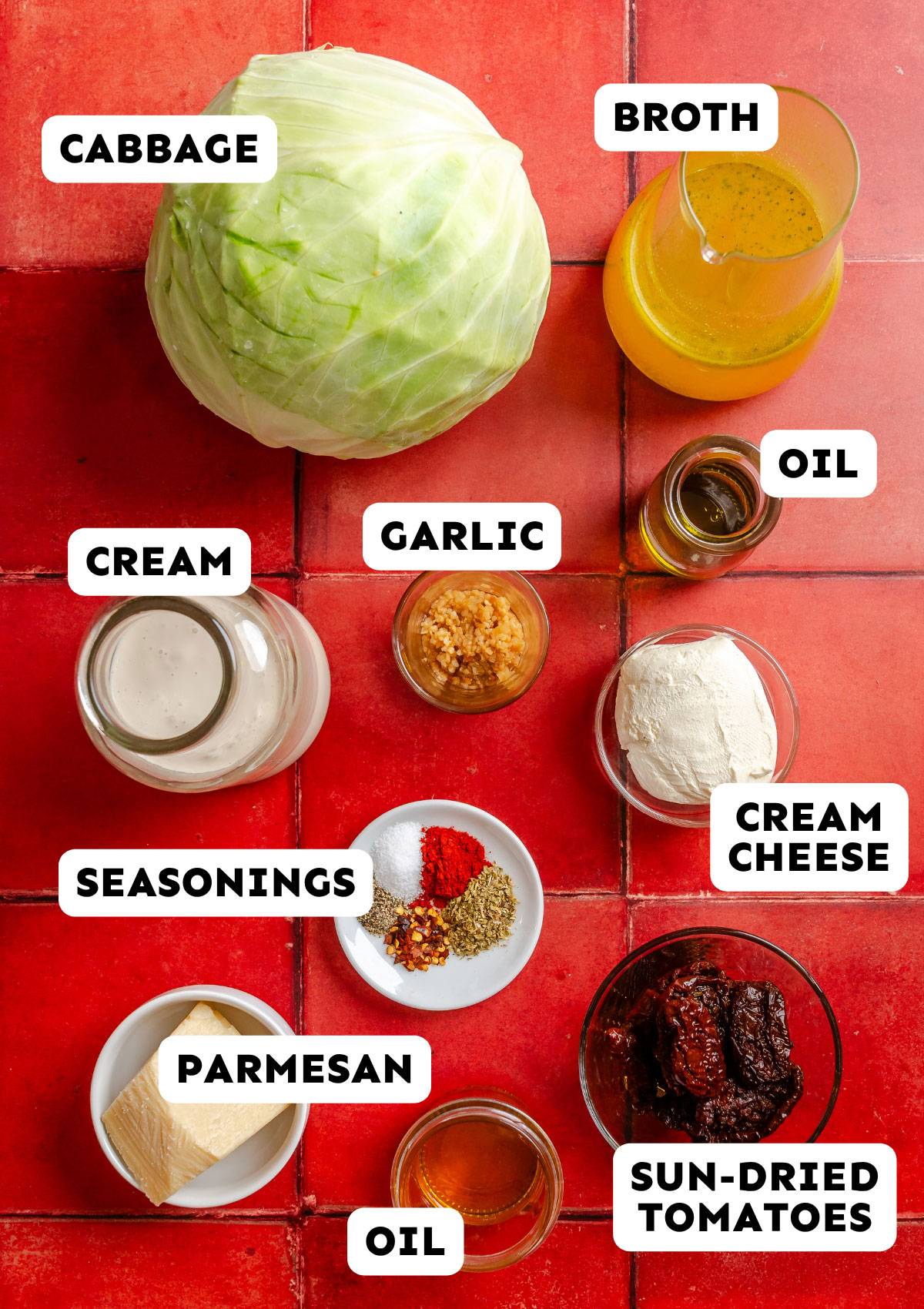 Cabbage, broth, cream, cream cheese, garlic, oil, parmesan, sun-dried tomatoes, and seasonings—everything you need to create Marry Me Melting Cabbage—are beautifully arranged on a red tiled surface.