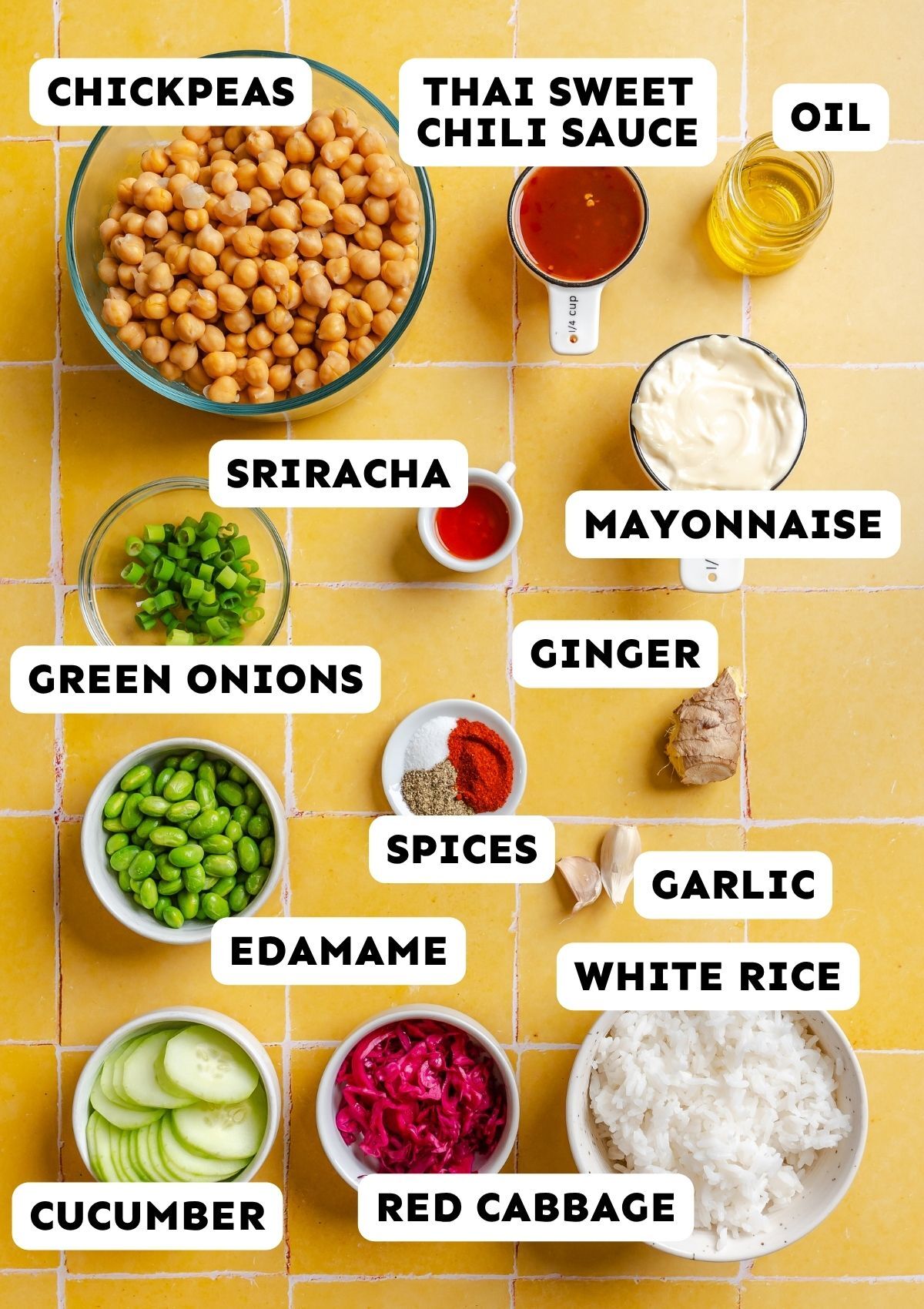 Ingredients for a rice bowl recipe are arranged on a yellow tiled surface, including chickpeas, sauces, vegetables, rice, spices, and oil, each labeled with text.