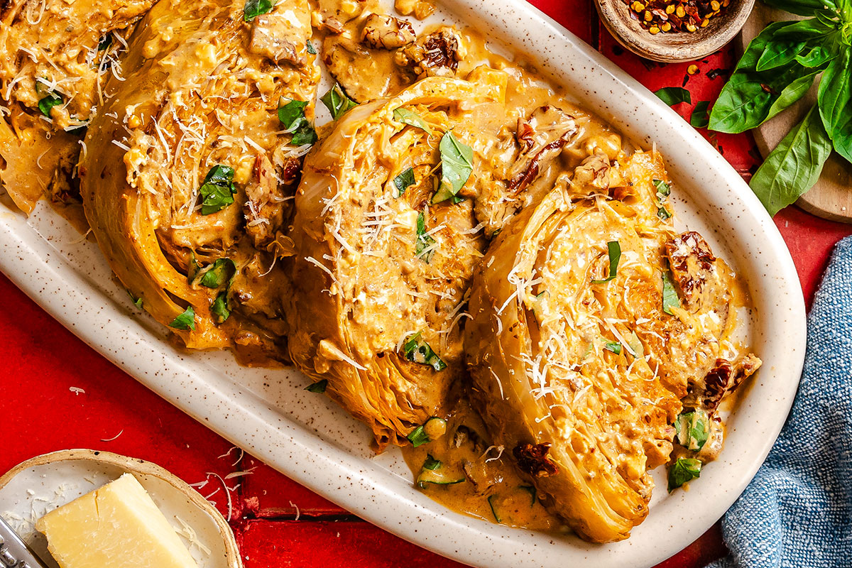 Three marry me cabbage steaks topped with creamy sauce, sun-dried tomatoes, and grated cheese are garnished with fresh basil on a white oval platter.